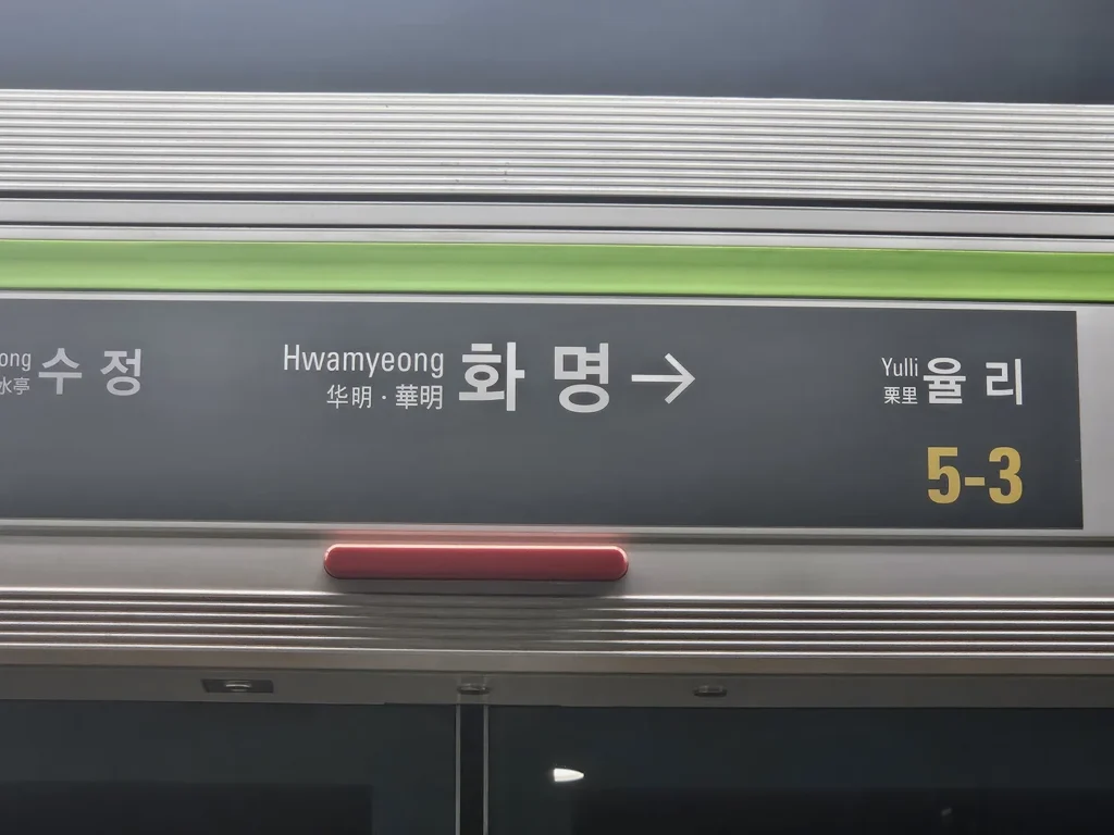 A Busan Metro Line 2 platform sign above a screen door showing Hwamyeong station, the previous stop Sujeong, the next stop Yulli, and the door number 5-3