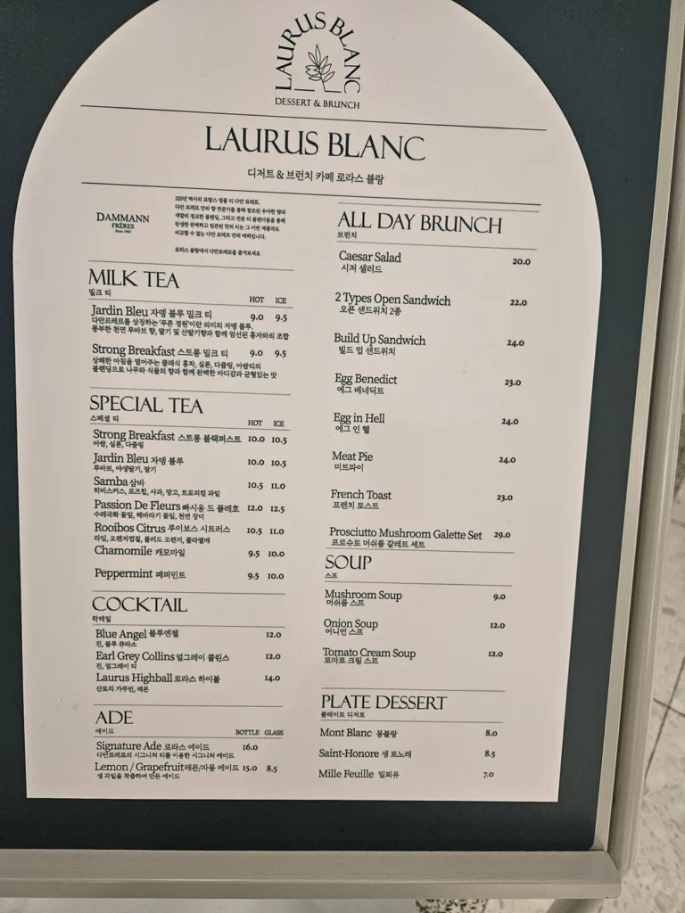 A bilingual menu board at a Korean brunch café with prices written in thousands of won, such as 9.5 for a milk tea and 20.0 for a Caesar salad