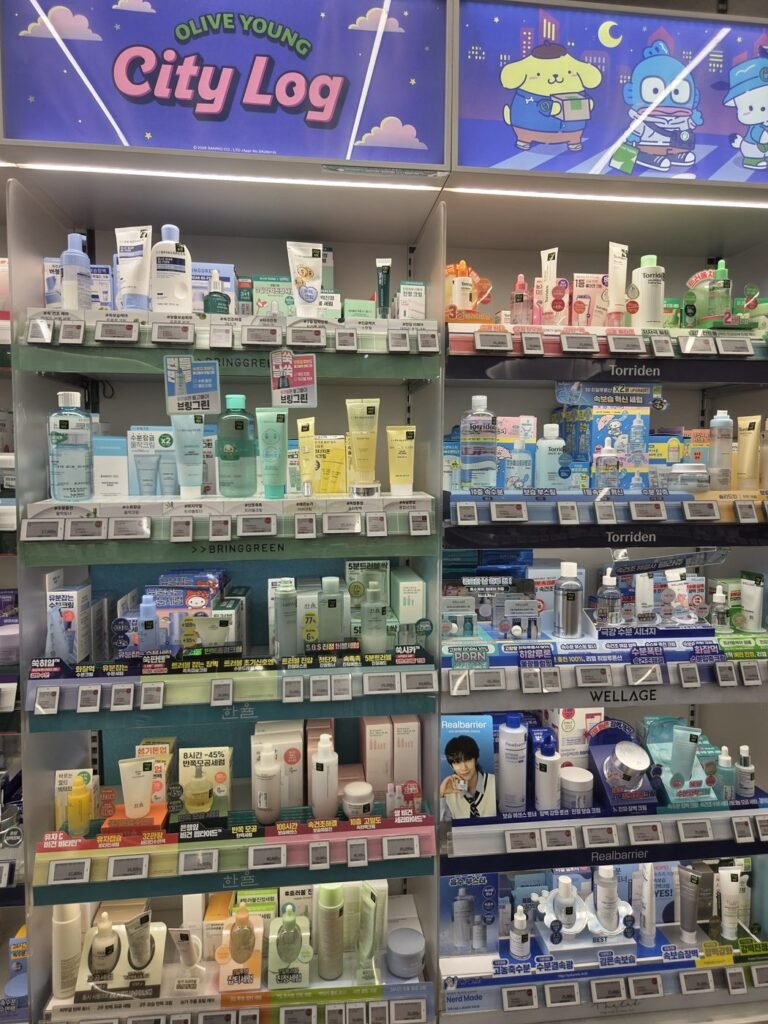 Olive Young skincare wall under cartoon-character banners reading Olive Young City Log, with Torriden and Wellage sections