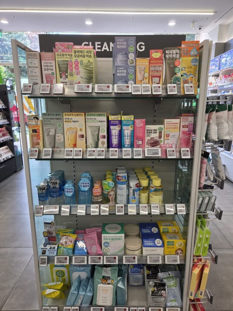 Olive Young cleansing aisle under a CLEANSING sign, with pack cleansers, foams, oils, cleansing waters, pads and wipes on five shelves
