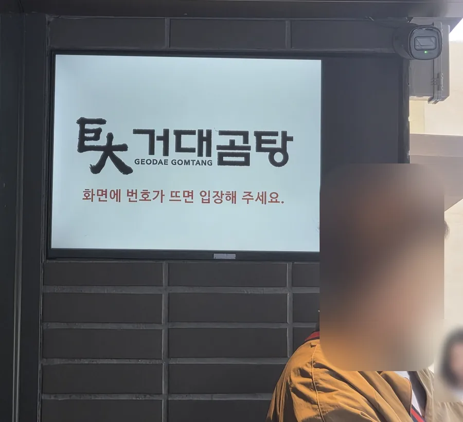 The screen above the entrance of Geodae Gomtang reading 화면에 번호가 뜨면 입장해 주세요 — when your number appears on the screen, please come in
